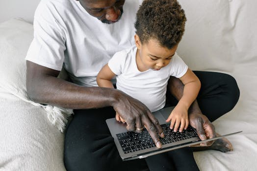 A father and child sitting together on a couch using a laptop for entertainment or education.