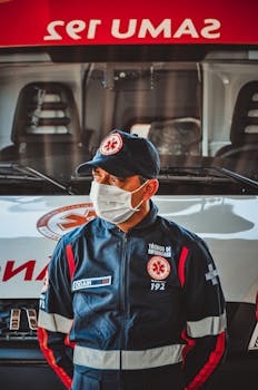 A masked emergency medical technician stands in front of an ambulance, ready for action.